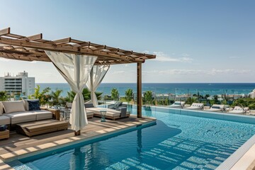 A large swimming pool area with a modern couch overlooking the vast ocean - obrazy, fototapety, plakaty