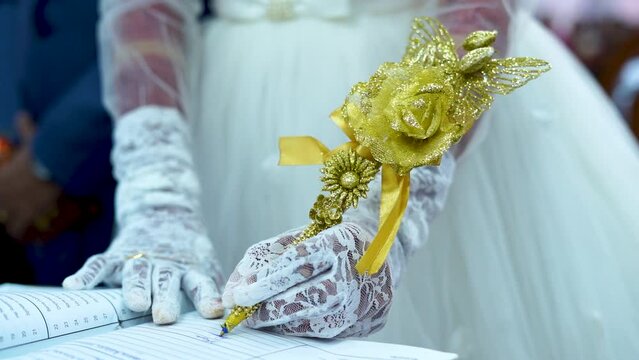 A bride signs the marriage contract using an elegantly decorated pen in gold.