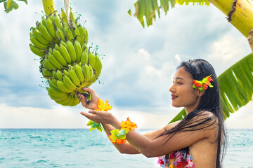 Hawaiian hula dancer holding a bunch of bananas growing on a palm tree