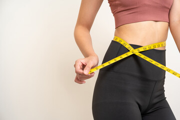 Close up woman measuring her waistline with measure tape. Weight loss diet session. Woman in sportswear slim fit and firm body shape. Care about eating and workout exercise.