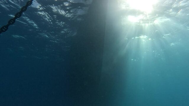 Sun rays sparkle in water on side of boat with strong dark shadow from hull