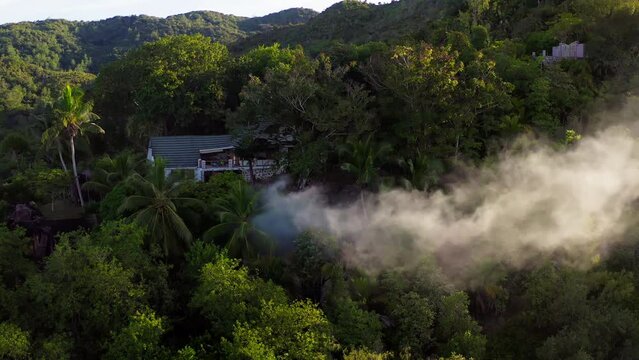 Drone shot captures big plumes of smoke coming from a property on top of a mountain.  Burning trash is a common practice on islands. Solid waste management in small islands is often challenging.