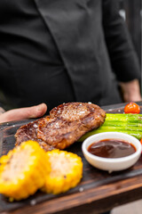 well-grilled steak with grill marks, served on a wooden board. Accompanying the steak are bright...