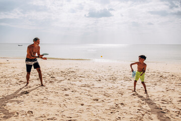 Shirtless man and son playing beach tennis near sea on vacation