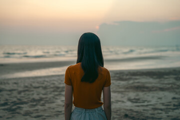 A sad and stressed Asian woman stands alone on the beach in the evening. Dramatic atmosphere....
