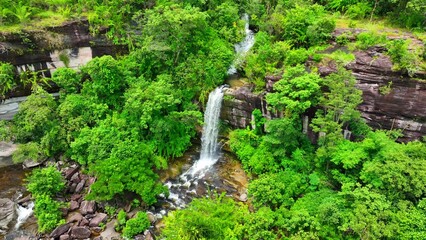 Lush green canopy surrounds a majestic tropical waterfall, seen from above in all its natural splendor. Soi Sawan Waterfall, Pha Taem National Park, Ubon Ratchathani Province, Thailand. 
