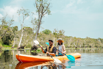 Holiday travel activities. Happy asian couple man and woman rowing a canoe or kayak in mangrove...