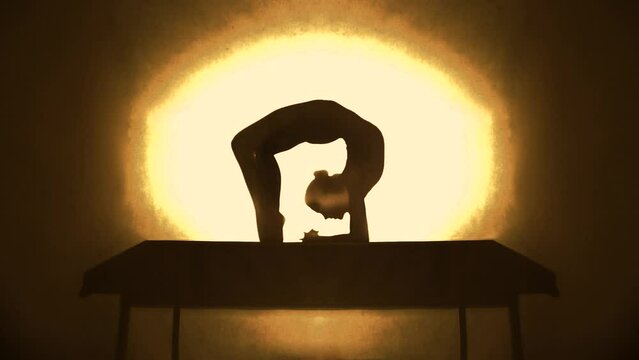 Silhouette of contortionist woman bending before yellow spotlight