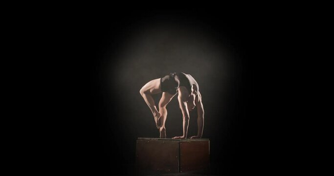 Spotlight on female acrobat in backbend on box straightening leg, performance