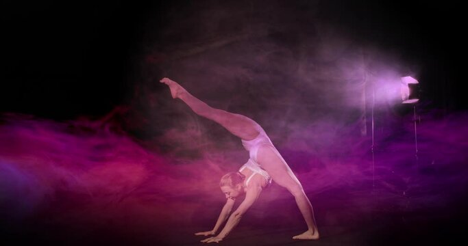 Acrobat do artistic flexible floor moves on stage with spotlight and pink smoke