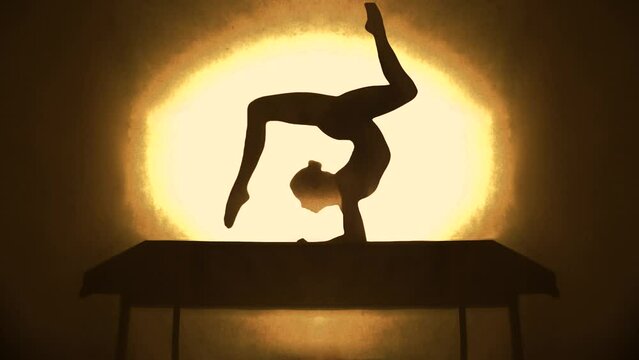 Silhouette of a woman doing yoga positions in front of a yellow light. 