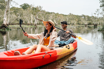 Holiday travel activities. Happy asian couple man and woman rowing a canoe or kayak in mangrove forests. Young traveler with kayak at botanical garden tropical mangrove forest in a national park.