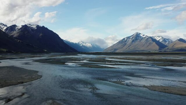 Braided glacial river flowing through wide valleys and across rocky landscapes in New Zealand. Low to the ground aerial.