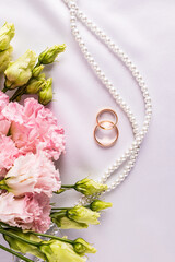 Beautiful wedding vertical background with two gold rings, pearl beads, pink austoma flowers. Top view. Greeting card, invitation, mockup.