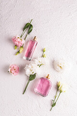 Two different bottles of women's perfume with a floral fragrance on a white textured background among flowers. Top view. Flat lay. Perfume concept.
