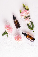 Top view of cosmetic bottles made of dark glass with a pipette with a natural facial skin care product. . Flat lay. White Textured background, flowers