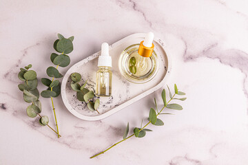 Natural cosmetic eucalyptus oil in a bowl and cosmetic bottle on an oval tray among eucalyptus twigs. Top view. Natural cosmetics.