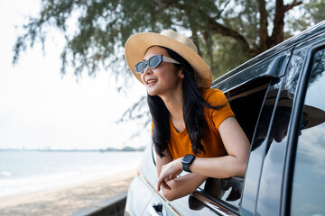 A young beautiful asian woman travel to the sea by car on a bright day. With beautiful blue sky. Vacation holiday weekend after hard work. Sticking her head outta the windshield