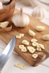 Aromatic cut garlic, cloves and bulbs on white wooden table, closeup