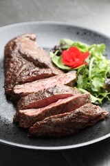 Pieces of delicious grilled beef meat and greens on table, closeup