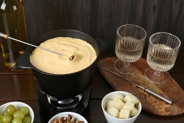Fondue pot with tasty melted cheese, forks, wine and different snacks on wooden table
