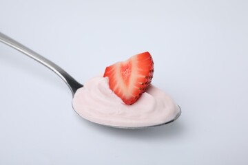 Delicious natural yogurt with fresh strawberry in spoon on light background