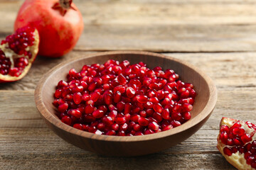 Ripe juicy pomegranate grains in bowl on wooden table, closeup