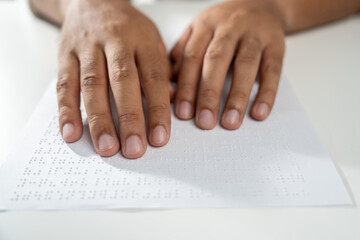 Hand of a blind person reading some braille text on page paper to learn. Finger of blind student...