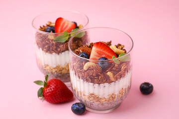 Tasty granola with berries, nuts, yogurt and chia seeds in glasses on pink background