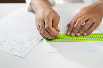 Close up Hand of a blind person writing some braille text on page paper. Young blind man using...