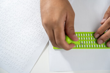 Close up Hand of a blind person writing some braille text on page paper. Young blind man using...