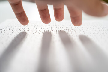 Hand of a blind person reading some braille text on page paper to learn. Finger of blind student touching the braille alphabet Code on sheet.
