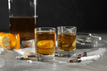 Alcohol and drug addiction. Whiskey in glasses, syringes, pills and cocaine on grey table