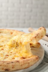Taking piece of delicious cheese pizza at table, closeup