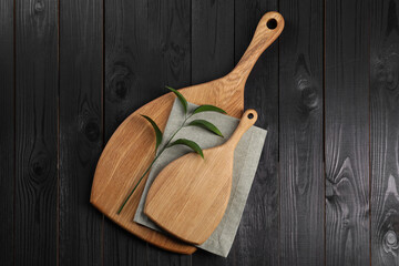 Cutting boards, green branch and napkin on black wooden table, top view