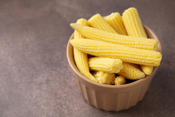 Tasty fresh yellow baby corns in bowl on brown table, closeup. Space for text