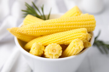 Tasty fresh yellow baby corns in bowl on white table, closeup