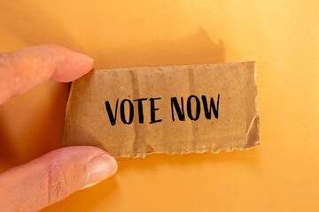 Vote now words written on ripped cardboard paper with orange background. Conceptual vote now...