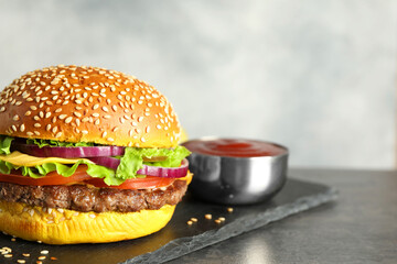 Burger with delicious patty and sauce on dark table against gray background, closeup