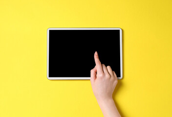 Online store. Woman using tablet on yellow background, top view