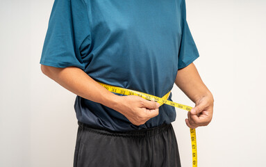 Senior man measuring waistline with measure tape. Weight loss diet session. Old man in sportswear fit and firm body shape. Care about eating and workout exercise. - Powered by Adobe