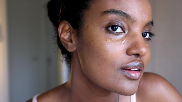 A pretty black African American woman wearing sleeveless top is placing eye serum for skin care routine in her room