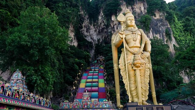 Murugan Statue With Colorful Staircase To Batu Caves In The Background. - wide shot