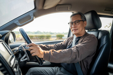 Senior Asian man drives a car vehicle on a clear day. With beautiful blue sky. He smiling driving...