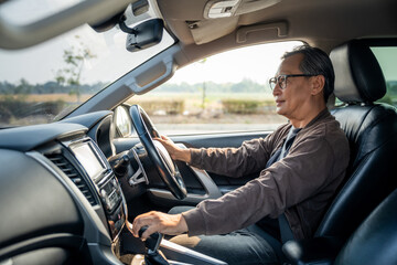 Senior Asian man drives a car vehicle on a clear day. With beautiful blue sky. He smiling driving...