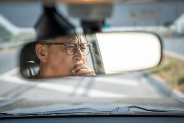 Rear view mirror. Senior asian man driver was drowsy. Mature old man yawned and was about to fall...