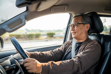 Senior Asian man drives a car vehicle on a clear day. With beautiful blue sky. He smiling driving to travel by car. Old man getting new car.