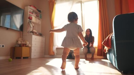 baby toddler first steps. baby daughter takes the first steps around the room to his parents sitting by the window glare of sun learns to walk. happy family kid concept. toddler first steps dream