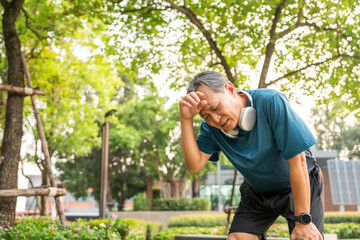 Senior asian man tired during jogging at outdoor nature park. Mature asian male intense training...