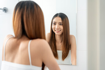 Self confident women look in the mirror brush up their hair and admire their body. Young asian...